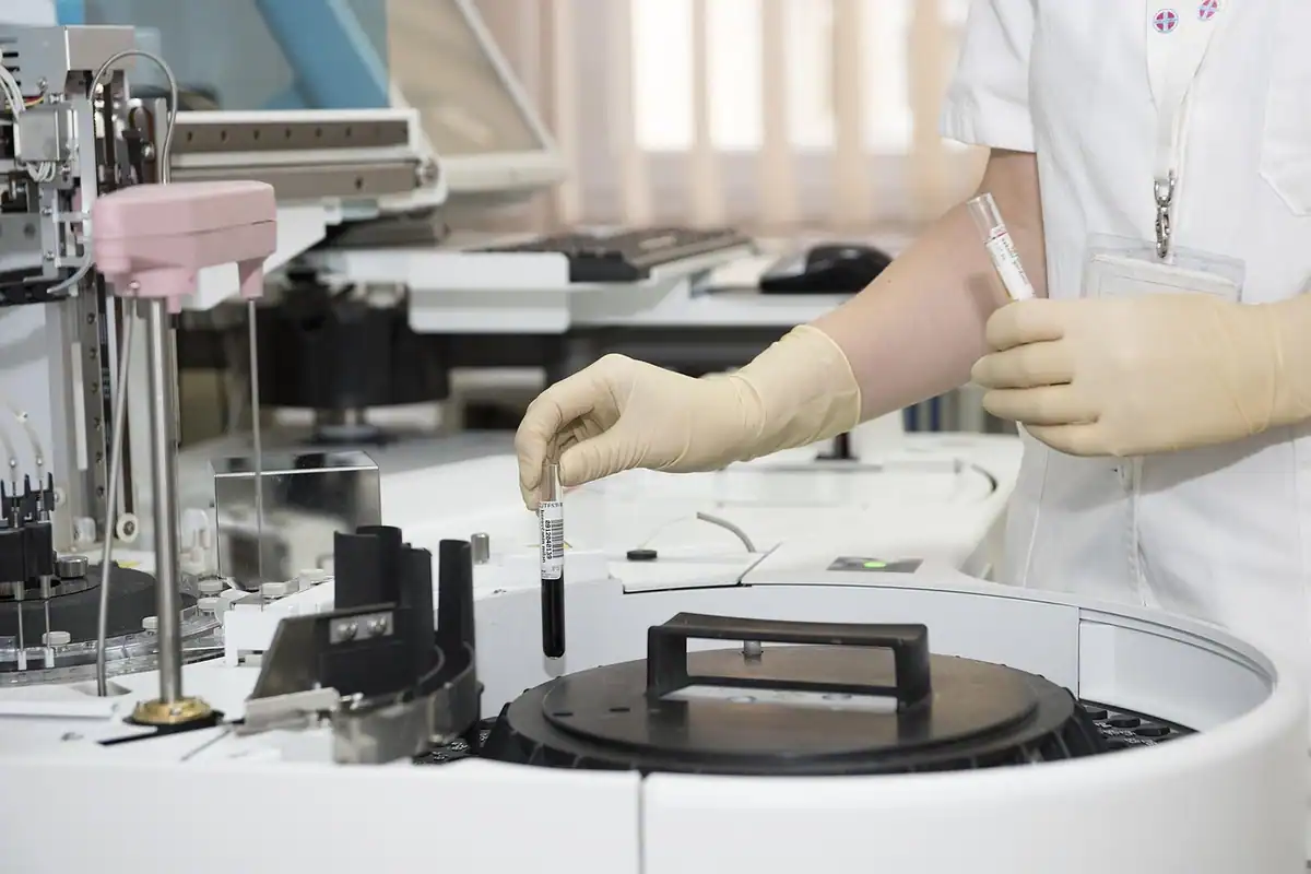 Laborantă cu mănuși care pune eprubete cu ser în centrifuga unui laborator de biochimie