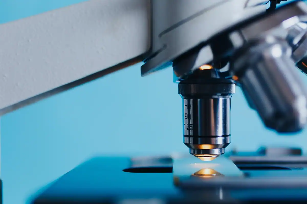 Obiectivul unui microscop deasupra unei lame, folosit la examinarea probelor de laborator