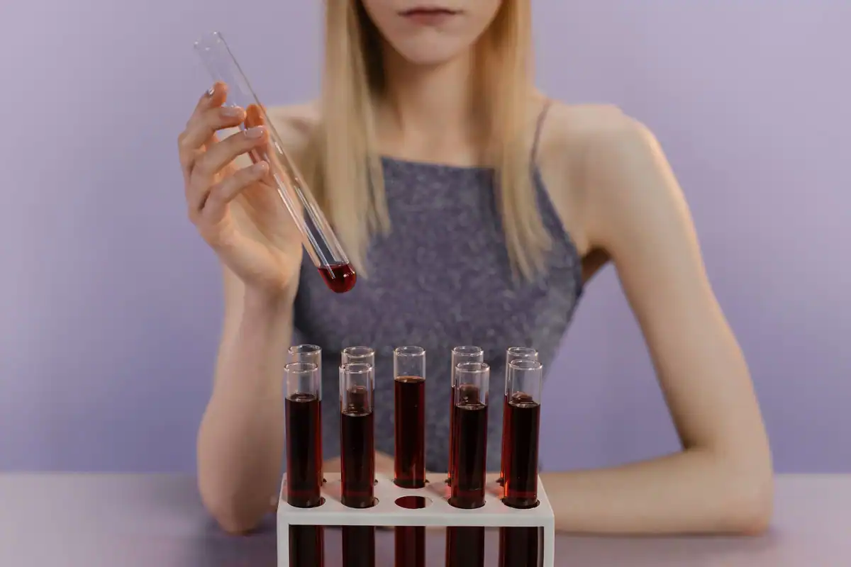 Tânără care ține o eprubetă cu sânge, lângă un suport cu probe pentru testele hepatice