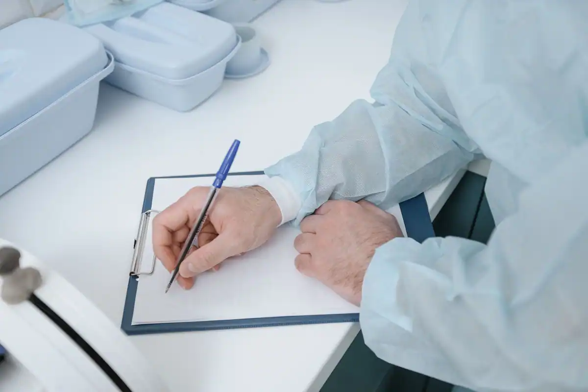 Medic în echipament de protecție care completează fișa unui pacient pe un clipboard