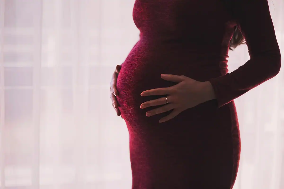 Mâini așezate pe burta unei femei însărcinate, într-o lumină blândă de interior