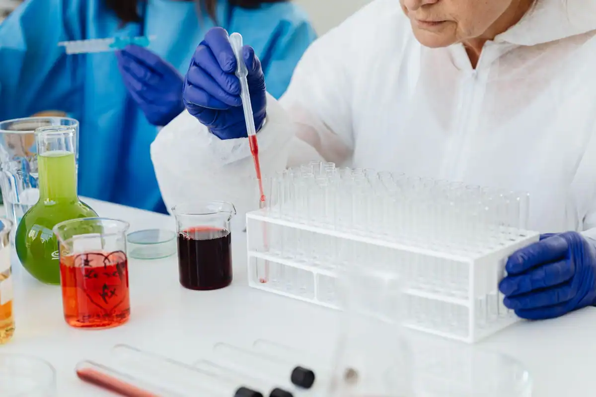 Cercetătoare în halat alb care folosește o pipetă pe eprubete cu soluții colorate