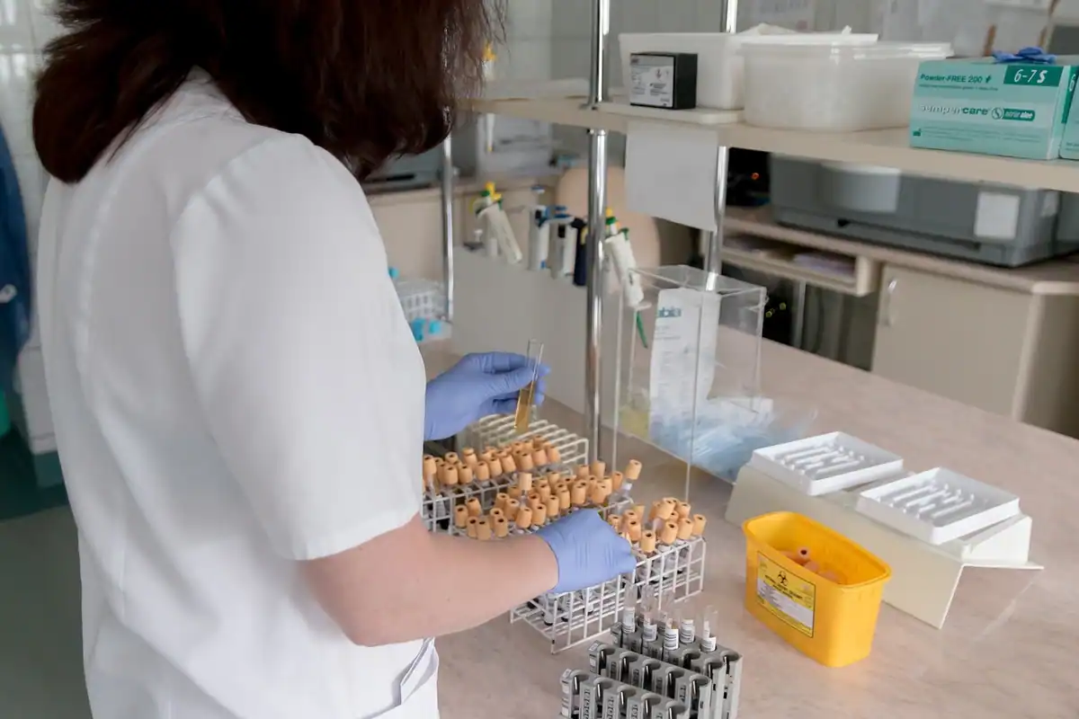 Laborantă care sortează probe de sânge în suporturi pe masa laboratorului