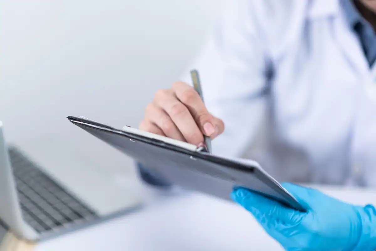Medic cu mănușă albastră care completează pe clipboard un rezultat de analiză