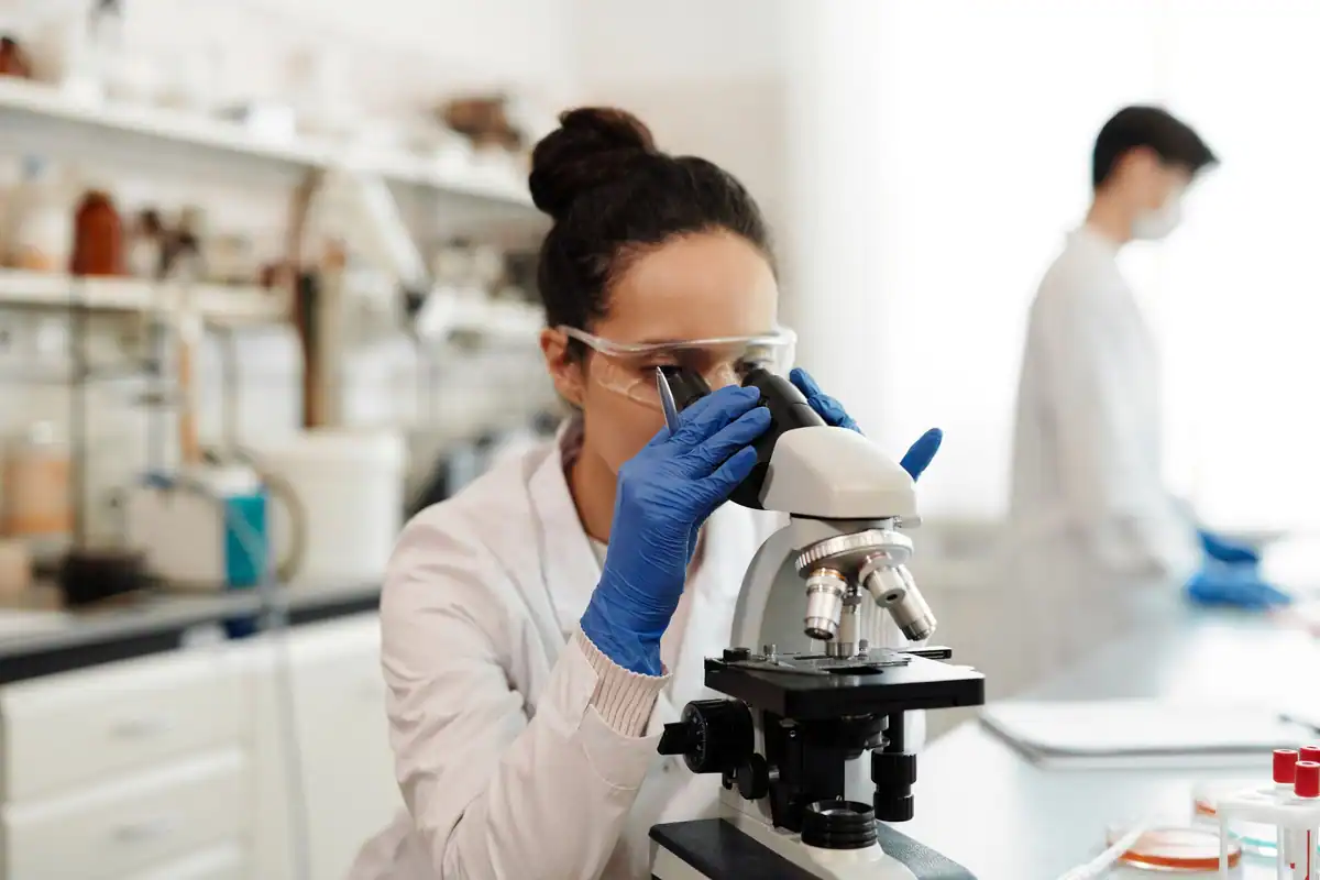 Cercetătoare în echipament de protecție care privește o probă la microscop