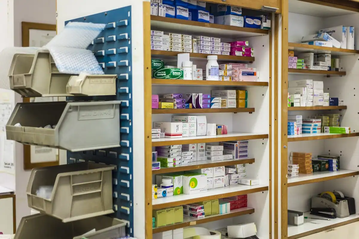 Rafturi de farmacie cu cutii de medicamente aranjate pe categorii, într-o încăpere luminoasă