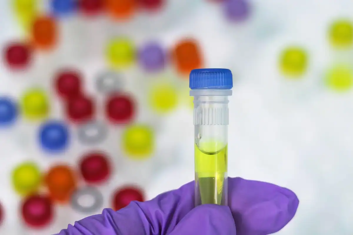 Eprubetă cu lichid galben ținută în mână, printre bile colorate din laborator